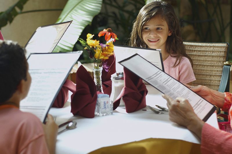 Niña leyendo la carta para luego escoger su plato. Créditos de la foto: Internet